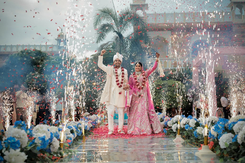 Bride and groom walk amid fireworks in a vibrant outdoor Indian wedding ceremony.