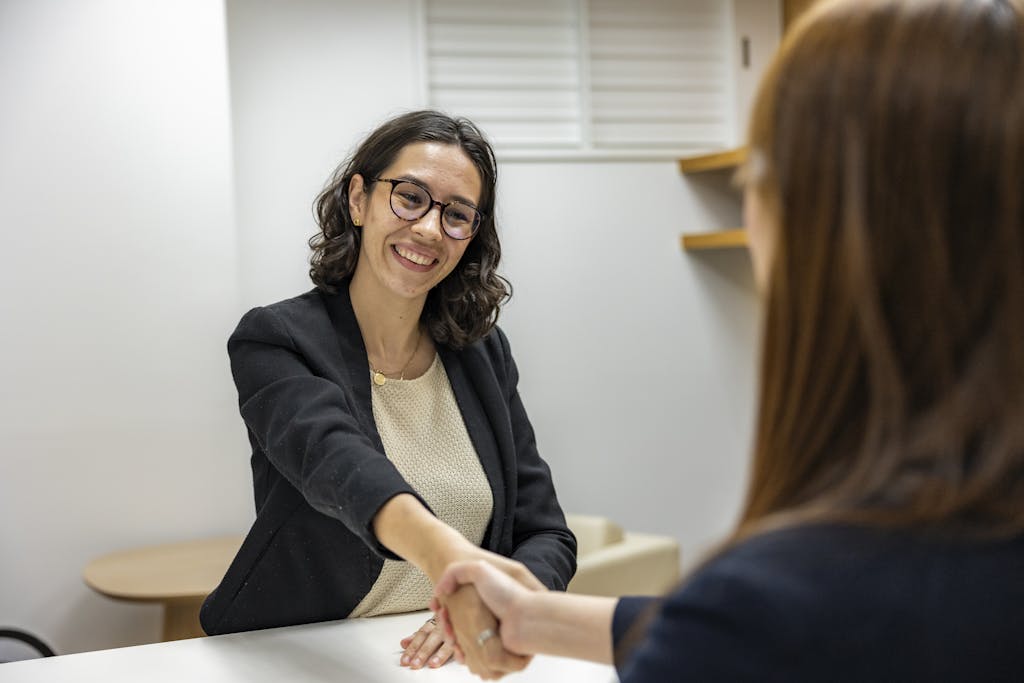 Businesswomen shaking hands in an office, representing a successful client meeting.