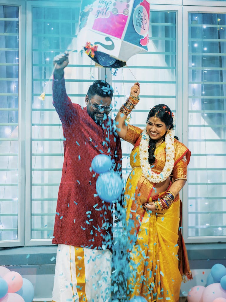 Happy couple at a vibrant gender reveal party indoors with blue confetti.