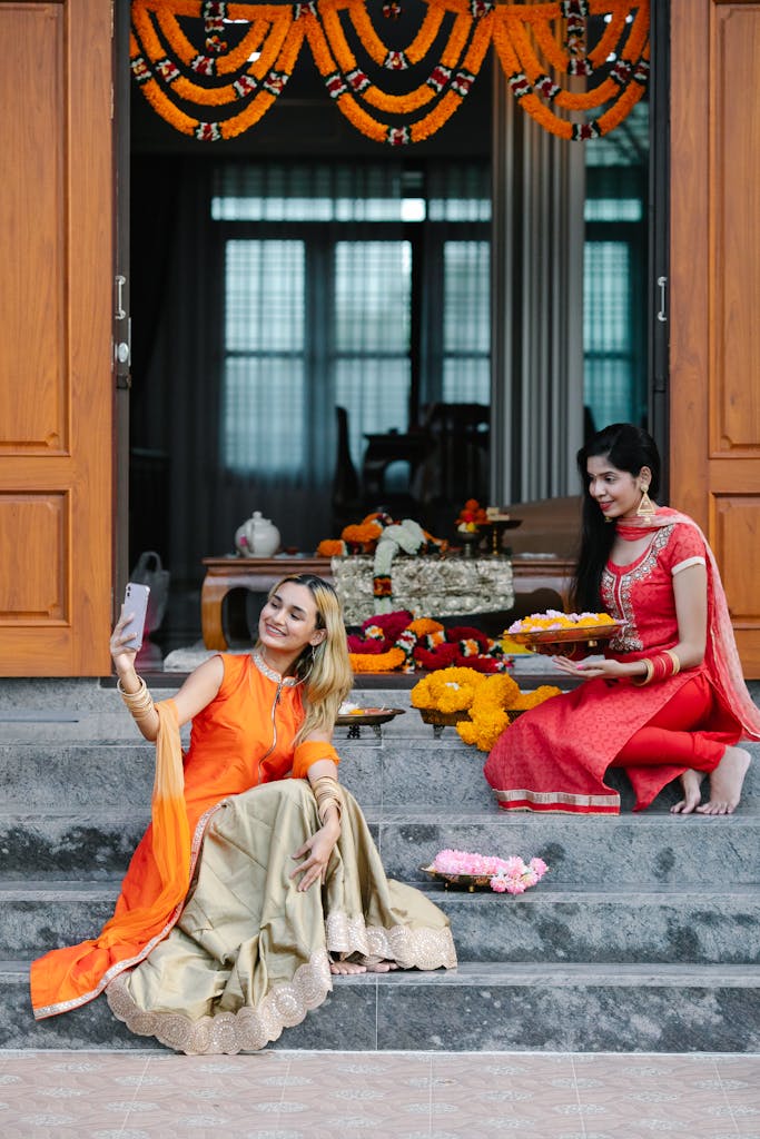 Two women in traditional Indian attire during a ceremony, capturing a moment with a smartphone.