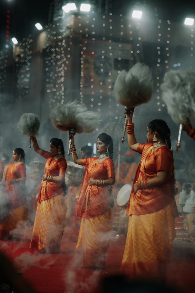 Women performing a traditional dance in vibrant attire during a cultural festival with smoke effects.