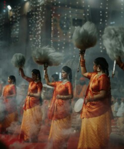 Women performing a traditional dance in vibrant attire during a cultural festival with smoke effects.