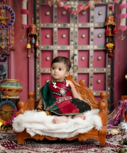 Adorable baby in traditional Indian attire surrounded by vibrant cultural decor.